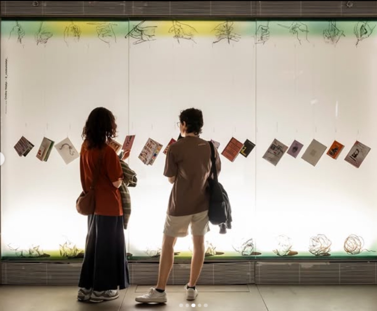 Dos personas miran fanzines colgados en un escaparate iluminado
